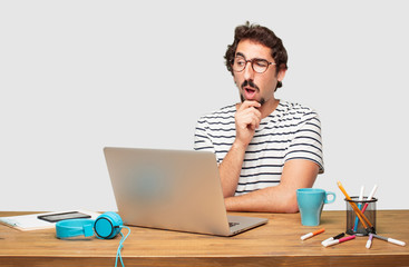 young bearded graphic designer with a laptop with a goofy, dumb, silly look, feeling shocked and...