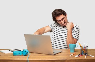 young bearded graphic designer with a laptop with an angry, aggressive and menacing pose, ready for...