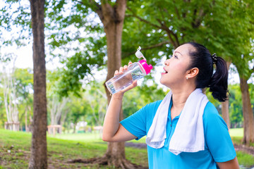 Asian woman relax time after jogger in park. She is drinking water. Life style,Photo concept  exercise and healthy.