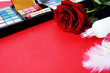Valentine's Day on a red background a red rose with jewelry, a bottle of perfume and cosmetics.