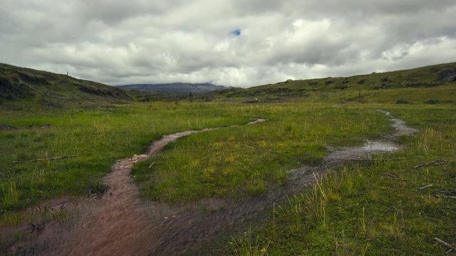 Time-lapse of muddy floodwater running over the paramo. Cotopaxi Volcano, partially hidden in the clouds in the distance. In the Andes, Ecuador.