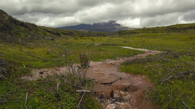Time-lapse of muddy floodwater running over the paramo. Cotopaxi Volcano, partially hidden in the clouds in the distance. In the Andes, Ecuador.