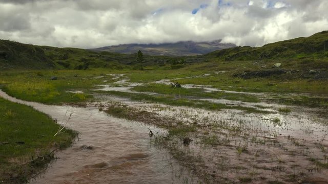 Time-lapse of muddy floodwater running over the paramo. Cotopaxi Volcano, partially hidden in the clouds in the distance. In the Andes, Ecuador.