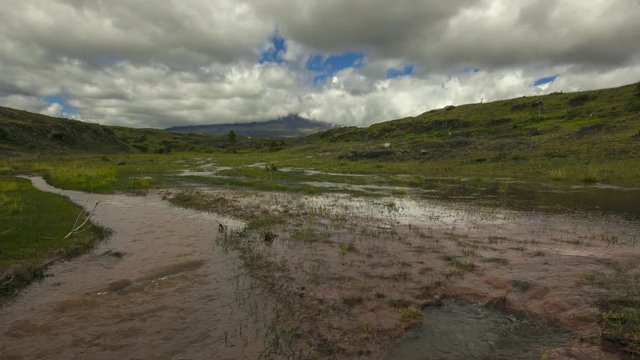 Time-lapse of muddy floodwater running over the paramo. Cotopaxi Volcano, partially hidden in the clouds in the distance. In the Andes, Ecuador.
