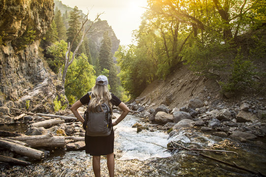 View from behind of a Woman hiking across a shallow mountain stream while on vacation in the Western United States. Candid photo of an active female enjoying the outdoors 
