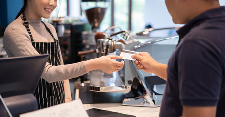 Asian women barista accept credit cards from customers in the coffee shop.