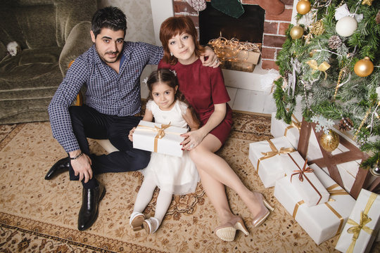 Family with Russian mom, Turkish dad and their daughter are in a room decorated for Christmas and new year