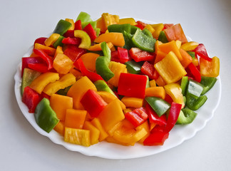 Sliced multicolor fresh Bulgarian pepper lies on a dish - vitamins and health benefits