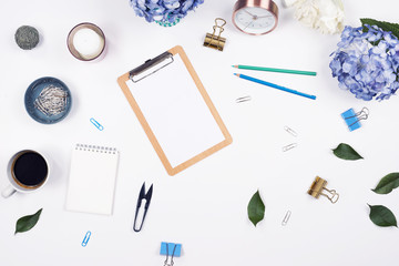 Feminine desk workspace frame mockup with beauty arrangement of bouquet hydrangeas, clipboard, notebook, pencil and candle on white background with copy space. Flat lay, Top view.