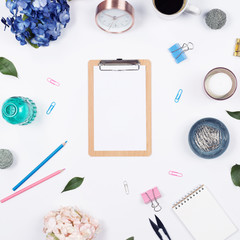 Feminine desk workspace frame mockup with beauty arrangement of bouquet hydrangeas, clipboard, notebook, pencil and candle on white background with copy space. Flat lay, Top view.
