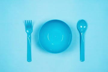 Set of empty blue plastic tableware bowls, spoons and forks  isolated on blue pastel background. Flat lay, Top view. Minimal style.