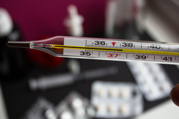a termometr with high temperature and different medicines on background