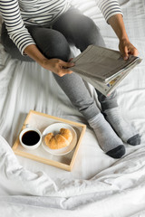 Woman reading book or newspaper and drinking coffee breakfast on bed during the morning