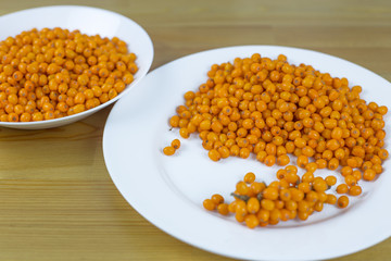Ripe sea buckthorn berries in white plates on the table