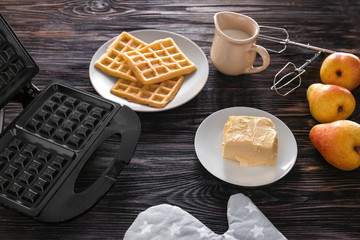 Belgian waffles with device and products on wooden table