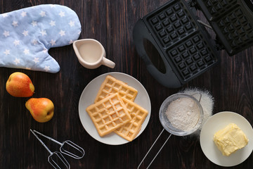 Belgian waffles with device and products on wooden table