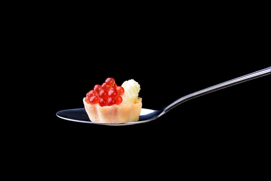 Tartlet with red caviar and butter on a tablespoon on a black background