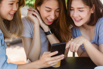 Cheerful asian young women sitting in cafe drinking coffee with friends and talking together. Attractive asian woman enjoying coffee while using smartphone for talking, reading and texting.