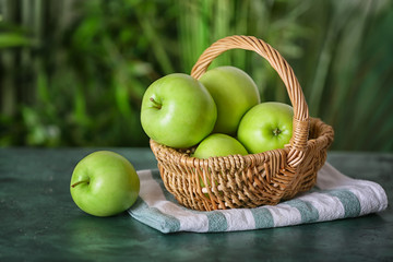 Basket with tasty green apples on color table