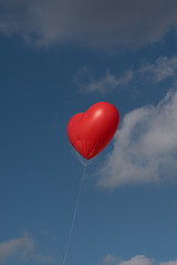 Fototapeta premium red heart balloon in front of blue cloudy sky 