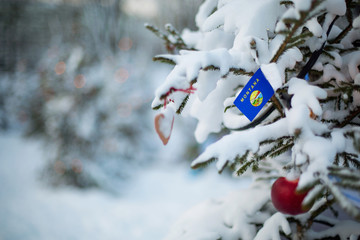 Montana state flag. Christmas background outdoor. Christmas tree covered with snow and decorations...