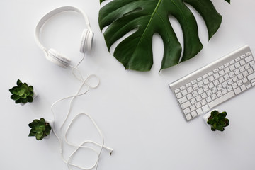 Headphones with computer keyboard and tropical leaf on white table