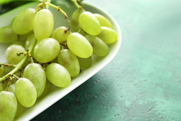 Plate with ripe juicy grapes on color table, closeup