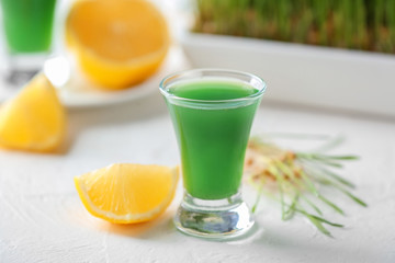 Glass of fresh wheat grass juice with lemon on table