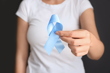 Woman holding blue ribbon on grey background, closeup. Cancer awareness concept
