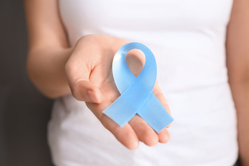Woman holding blue ribbon, closeup. Cancer awareness concept