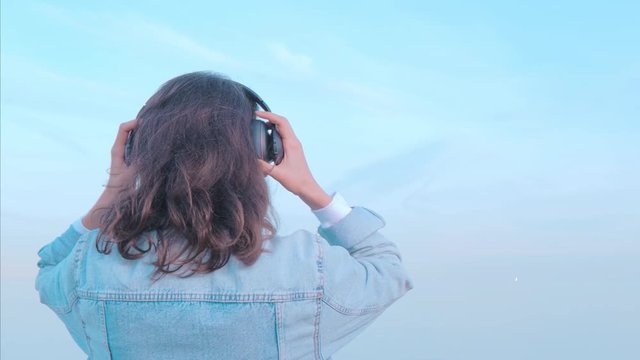 Woman in denim jacket sitting back and listening to music agains