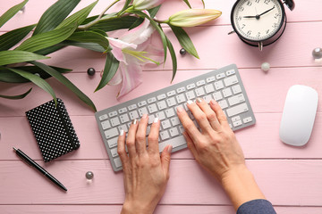 Woman using computer keyboard on color wooden table