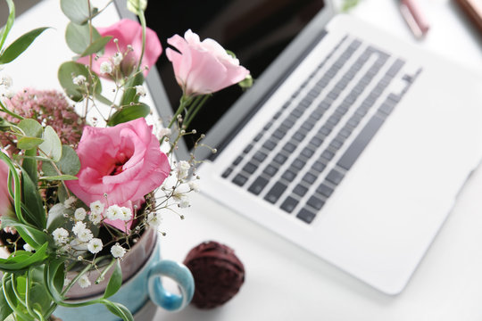 Vase with beautiful flowers and laptop on white table