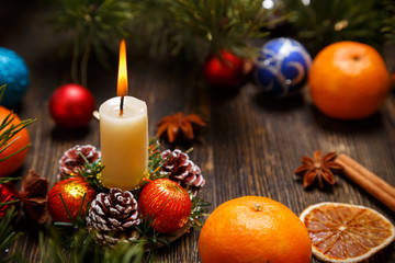 Fototapeta na wymiar Christmas decoration with the burning candle, tangerines, pine cones and balls on a wooden table, a copy space for your own text.