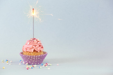 Delicious birthday cupcake with firework candle on color background