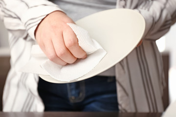 Woman wiping plate with paper towel in kitchen, closeup