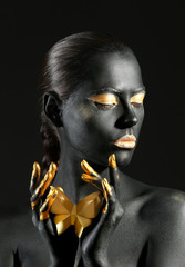 Beautiful woman with black and golden paint on her body against dark background - obrazy, fototapety, plakaty