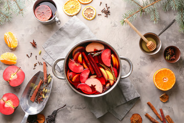 Saucepan and metal cup of delicious mulled wine with ingredients on grey table
