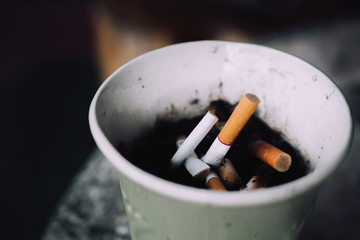 Burning cigarettes in ashtray on background. Area for smoking have cigarette stub on paper cup.