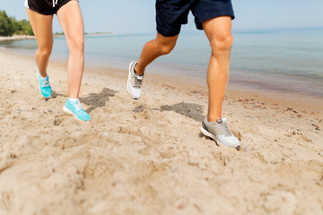 fitness, sport and technology concept - legs of couple of sportsmen in sneakers running along summer beach