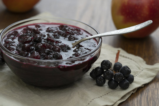 Home made black chokeberry and apple confiture in a glass jar on a wooden background.