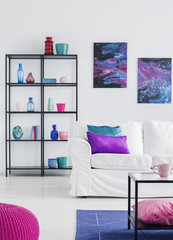 Pillows on white sofa in simple living room interior with posters of cosmos and glass table. Real photo