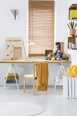 Blanket on chair at desk with yarns in white home office interior with blinds at windows. Real photo