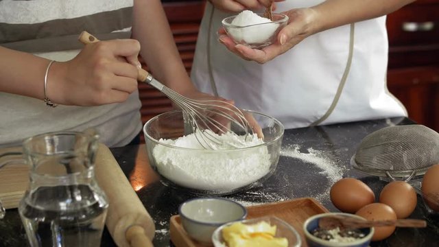 Hands of unrecognizable women adding sugar into bowl with sieved flour and whisking it while making cookie dough, close-up view