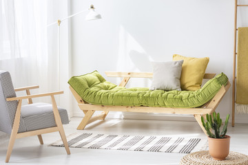 Patterned armchair and wooden green sofa in white living room interior with rug and plant. Real...