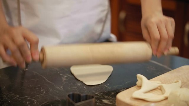 Close-up view of anonymous woman rolling cookie dough with wooden rolling pin on kitchen table