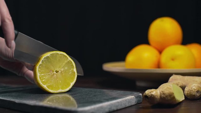 Lemon is cutted by sharp knife on the rock board, slices of fresh orange, fruit meal, vegetarian diet, making of fresh drink