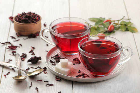 Hot red karkade tea in glass cups with dry tea on a white wooden table