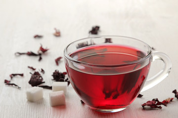 Hot red karkade tea in glass cups with dry tea on a white wooden table