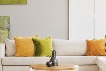 Yellow and green cushion on white settee in simple living room interior with wooden table. Real photo - Powered by Adobe